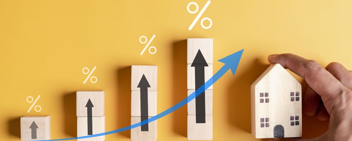 Illustration de l'augmentation des prix immobiliers, symbolisée par des blocs en bois, des pourcentages, une flèche bleue ascendante et une maison.