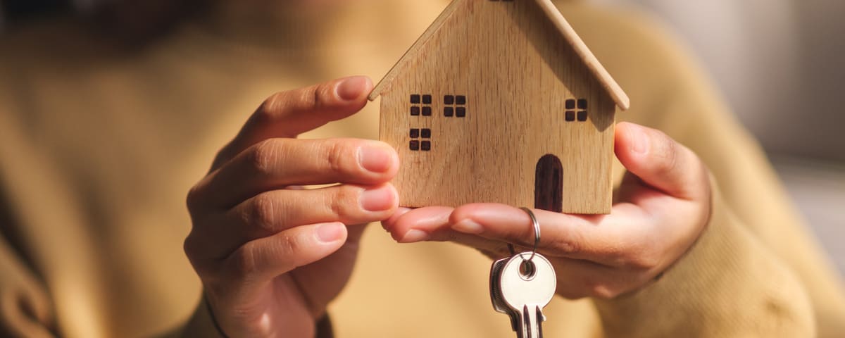 Personne tenant dans ses mains une maquette de maison en bois et des clés