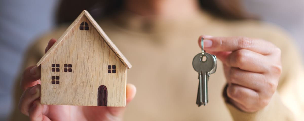 Une personne tenant une petite maison en bois miniature dans une main et une clé dans l'autre