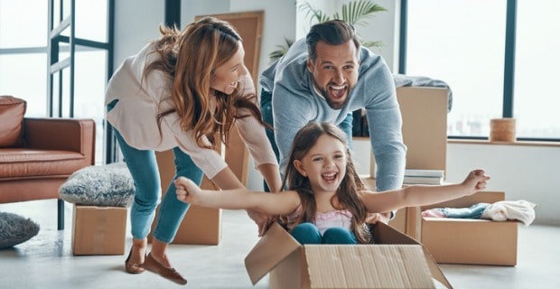 Jeune famille joyeuse qui prépare ses cartons. le papa et la maman poussent leure petite fille dans un carton